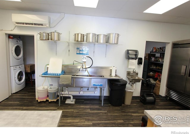 kitchen with stacked washing maching and dryer, dark wood-style floors, a drop ceiling, and a wall mounted air conditioner