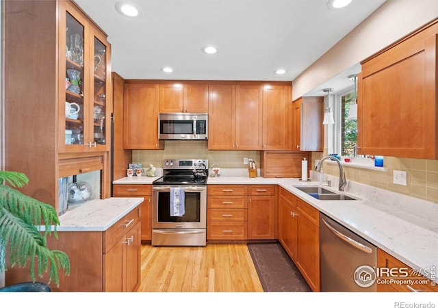 kitchen featuring stainless steel appliances, sink, backsplash, light stone counters, and light hardwood / wood-style flooring