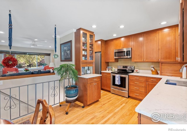 kitchen with ceiling fan, stainless steel appliances, backsplash, light wood-type flooring, and sink