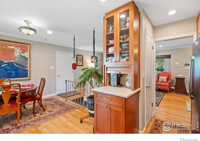 kitchen featuring light hardwood / wood-style floors, light stone counters, ornamental molding, and stainless steel refrigerator