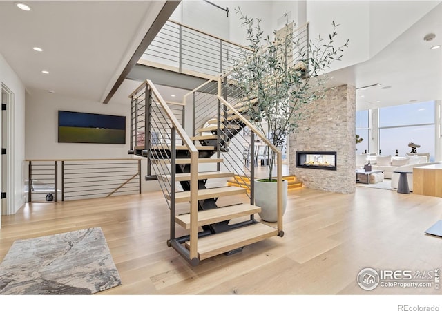 staircase with light hardwood / wood-style flooring, a stone fireplace, and a towering ceiling