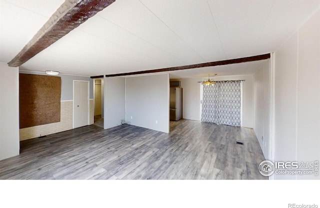 unfurnished room featuring beamed ceiling, an inviting chandelier, and wood finished floors