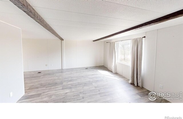 spare room featuring beam ceiling and light hardwood / wood-style flooring