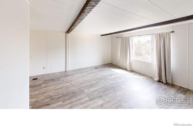 unfurnished room with beamed ceiling and light hardwood / wood-style flooring