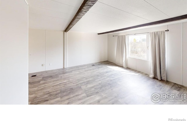 empty room featuring light wood-type flooring, visible vents, and beamed ceiling