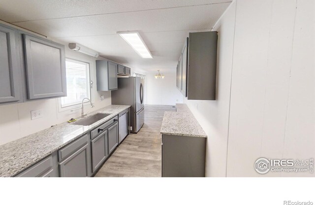 kitchen featuring gray cabinets, light wood-type flooring, sink, light stone counters, and appliances with stainless steel finishes