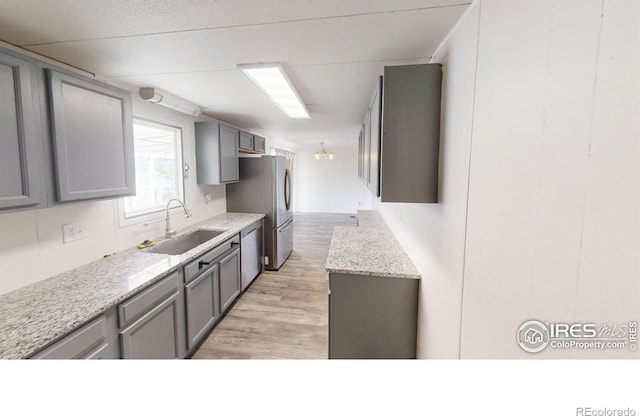 kitchen with light stone counters, light wood-style flooring, gray cabinetry, stainless steel appliances, and a sink