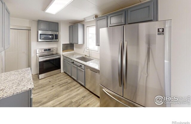 kitchen with light wood-type flooring, light stone counters, appliances with stainless steel finishes, sink, and gray cabinetry