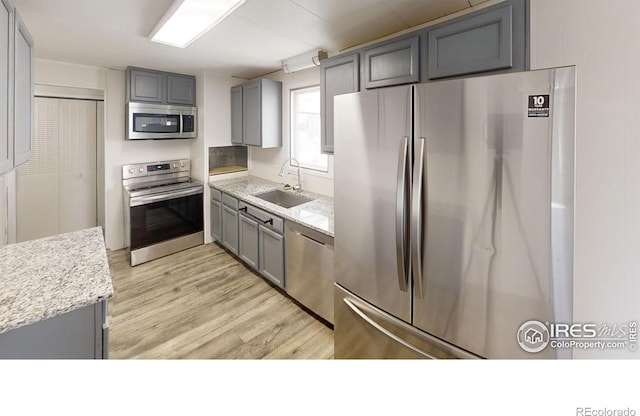 kitchen featuring appliances with stainless steel finishes, light wood-style floors, gray cabinets, and a sink
