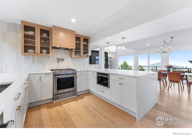 kitchen with decorative light fixtures, white cabinetry, stainless steel gas stove, backsplash, and kitchen peninsula