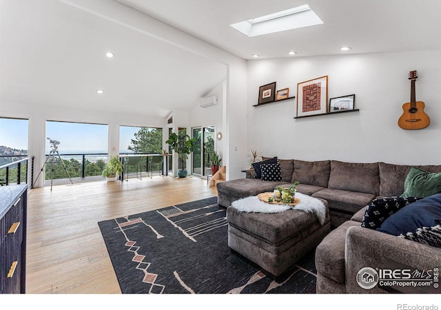 living room featuring light wood-type flooring, a wall mounted AC, and vaulted ceiling with skylight