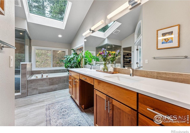 bathroom featuring vaulted ceiling with skylight, tiled tub, and vanity