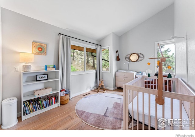 bedroom featuring multiple windows, wood-type flooring, a nursery area, and vaulted ceiling