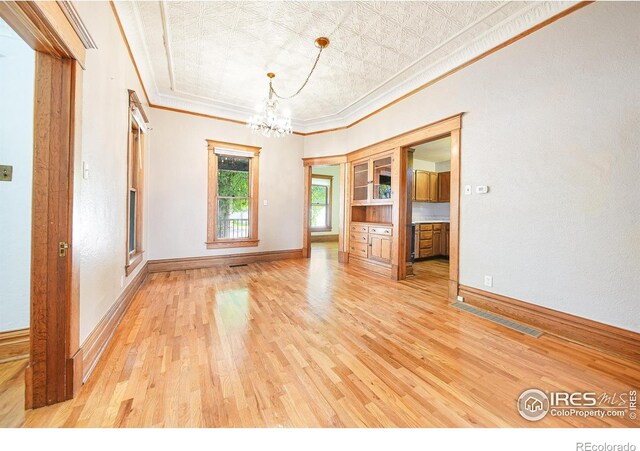 empty room with light hardwood / wood-style flooring, crown molding, and a chandelier