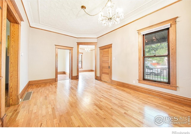 spare room featuring light wood-type flooring, a chandelier, a textured ceiling, and ornamental molding