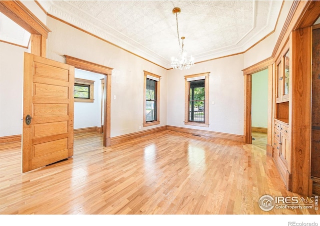 unfurnished room with an inviting chandelier, light hardwood / wood-style flooring, and ornamental molding