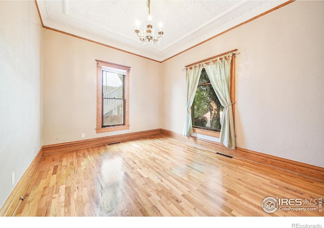 spare room featuring hardwood / wood-style flooring, crown molding, and an inviting chandelier