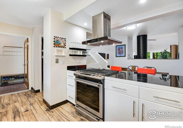 kitchen with white cabinets, tile counters, island range hood, light wood-type flooring, and gas range