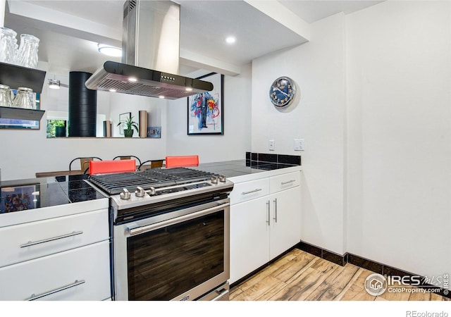 kitchen featuring tile countertops, stainless steel range with gas cooktop, white cabinetry, and island exhaust hood