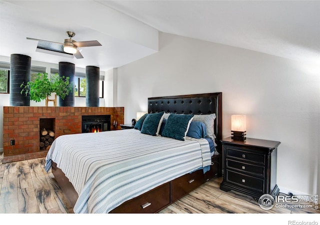 bedroom featuring ceiling fan, a brick fireplace, light hardwood / wood-style flooring, and lofted ceiling