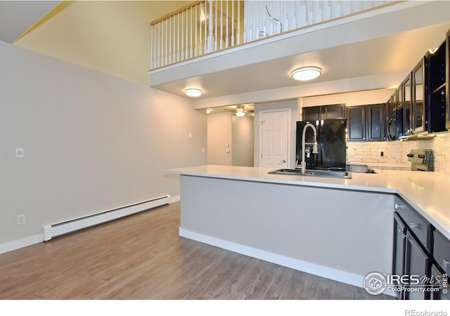 kitchen with a baseboard heating unit, light hardwood / wood-style floors, kitchen peninsula, decorative backsplash, and black appliances