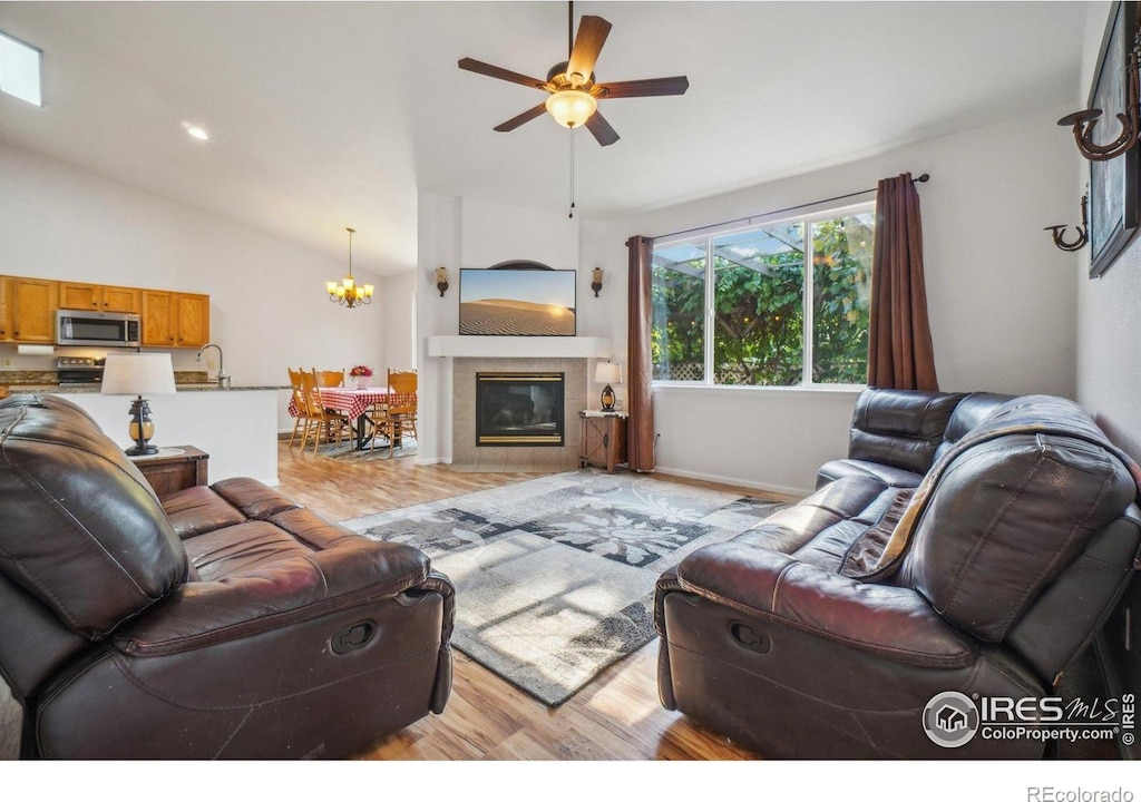 living room featuring lofted ceiling, light wood-type flooring, ceiling fan with notable chandelier, and a fireplace