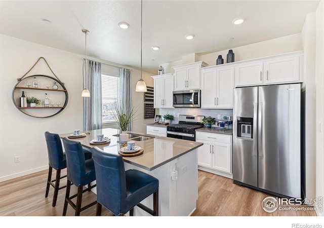 kitchen featuring pendant lighting, white cabinetry, stainless steel appliances, and a center island with sink