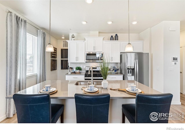 kitchen with a kitchen island with sink, pendant lighting, white cabinetry, and appliances with stainless steel finishes