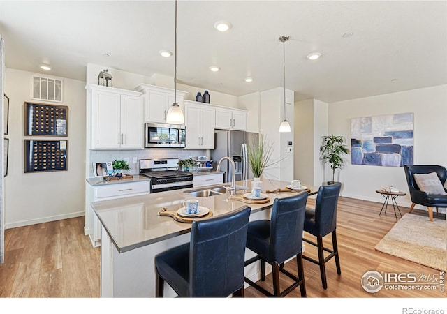 kitchen with appliances with stainless steel finishes, decorative light fixtures, sink, a kitchen bar, and a center island with sink