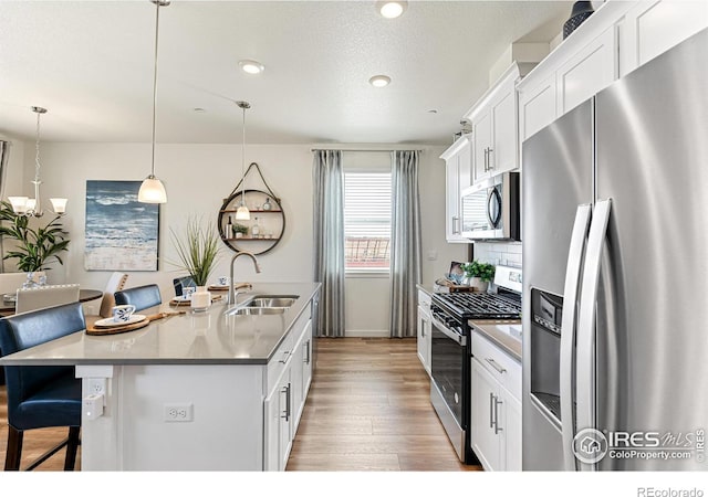 kitchen with pendant lighting, sink, white cabinetry, a kitchen island with sink, and stainless steel appliances