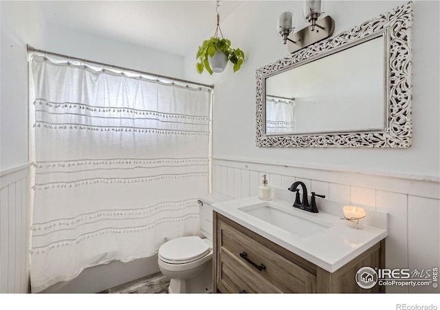 bathroom with curtained shower, wainscoting, vanity, and toilet