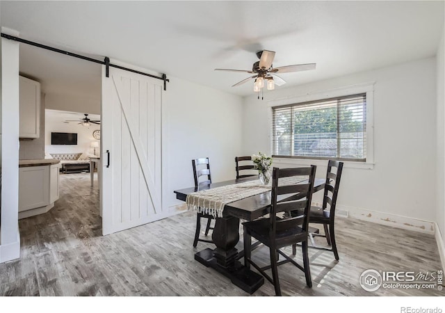 dining room with ceiling fan, a barn door, baseboards, and light wood-style flooring