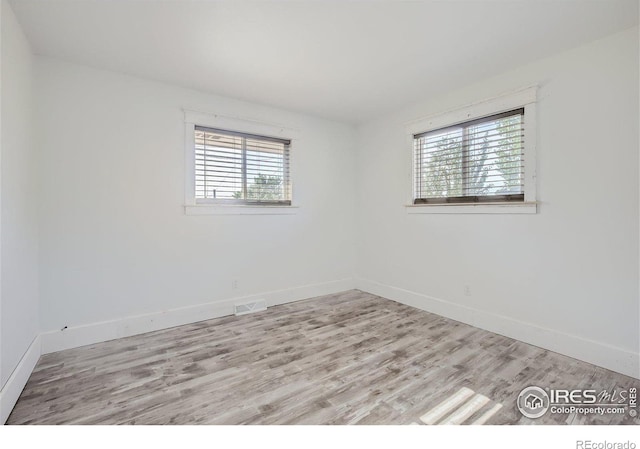 empty room featuring a healthy amount of sunlight, visible vents, baseboards, and wood finished floors