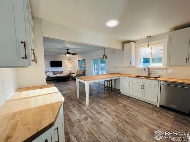 kitchen with butcher block countertops, a sink, open floor plan, stainless steel dishwasher, and tasteful backsplash