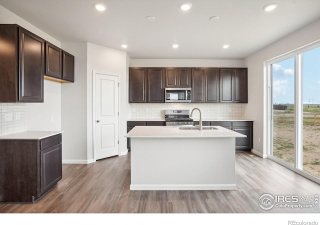 kitchen featuring light wood finished floors, appliances with stainless steel finishes, dark brown cabinets, and a sink