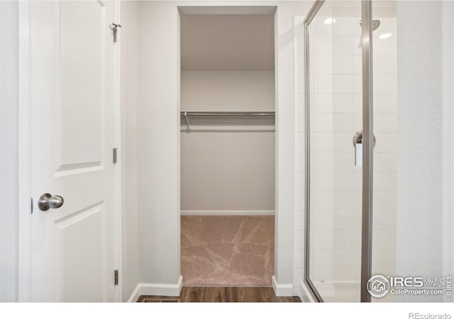 bathroom with a shower stall, baseboards, a walk in closet, and wood finished floors