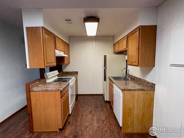 kitchen featuring white appliances, visible vents, dark wood-style floors, under cabinet range hood, and a sink