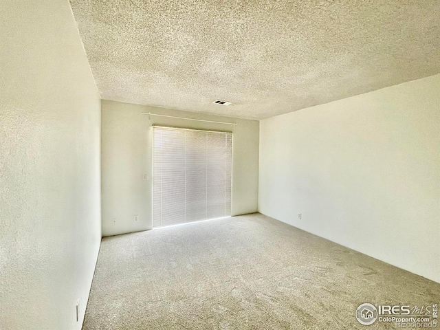 carpeted spare room featuring a textured ceiling, a textured wall, and visible vents