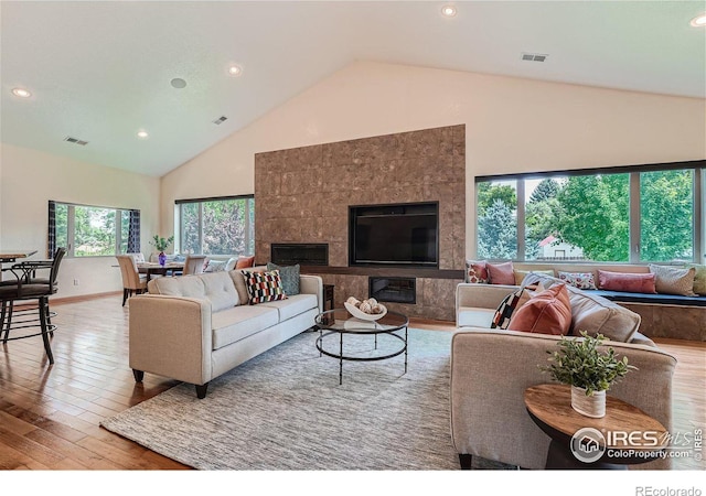 living room featuring a fireplace, high vaulted ceiling, and light wood-type flooring