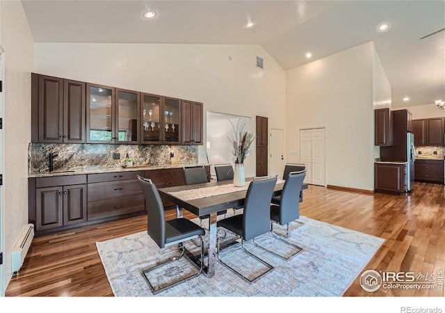 dining space featuring sink, dark wood-type flooring, high vaulted ceiling, and baseboard heating