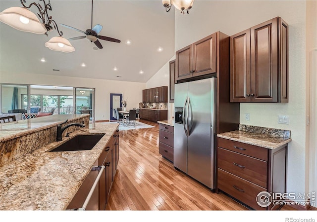 kitchen with light stone countertops, open floor plan, light wood-style floors, stainless steel appliances, and a sink