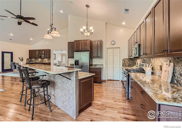 kitchen with appliances with stainless steel finishes, a spacious island, light stone counters, light hardwood / wood-style floors, and decorative light fixtures