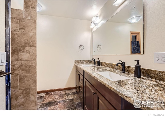 bathroom featuring a sink, baseboards, stone tile floors, and double vanity