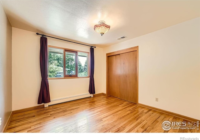 unfurnished bedroom with a closet, visible vents, light wood-type flooring, and a baseboard radiator