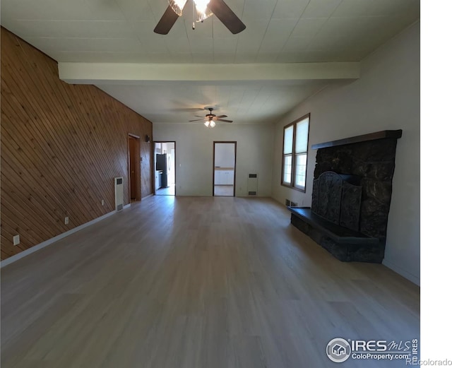 619 Curtis St, Brush, CO 80723 - unfurnished living room featuring beam ceiling, a ceiling fan, wood finished floors, wood walls, and a fireplace with raised hearth
