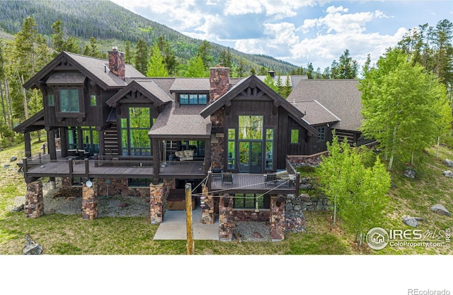 rear view of house with a shingled roof, stone siding, a patio, and a deck with mountain view