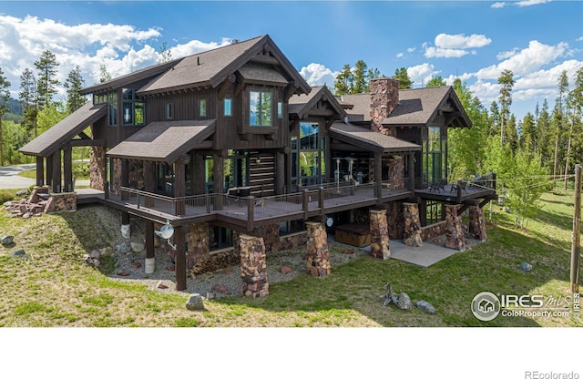 back of house featuring stone siding, a chimney, a wooden deck, and a lawn