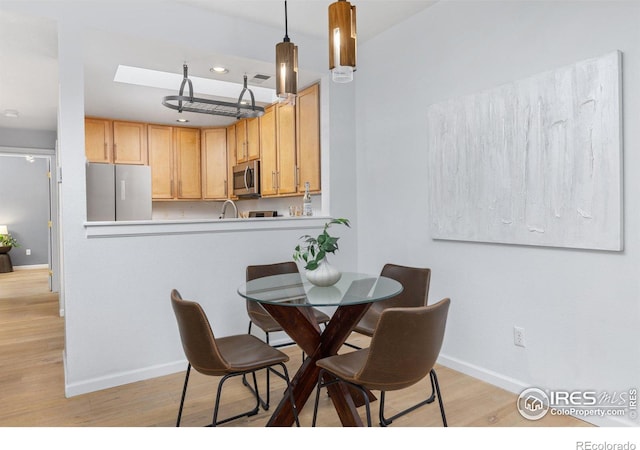 dining space featuring sink, light hardwood / wood-style flooring, and a skylight