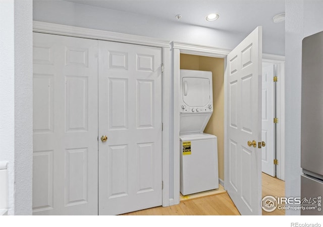 clothes washing area with light hardwood / wood-style flooring and stacked washer and clothes dryer