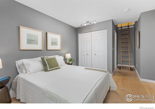 bedroom featuring track lighting, light wood finished floors, a closet, and baseboards